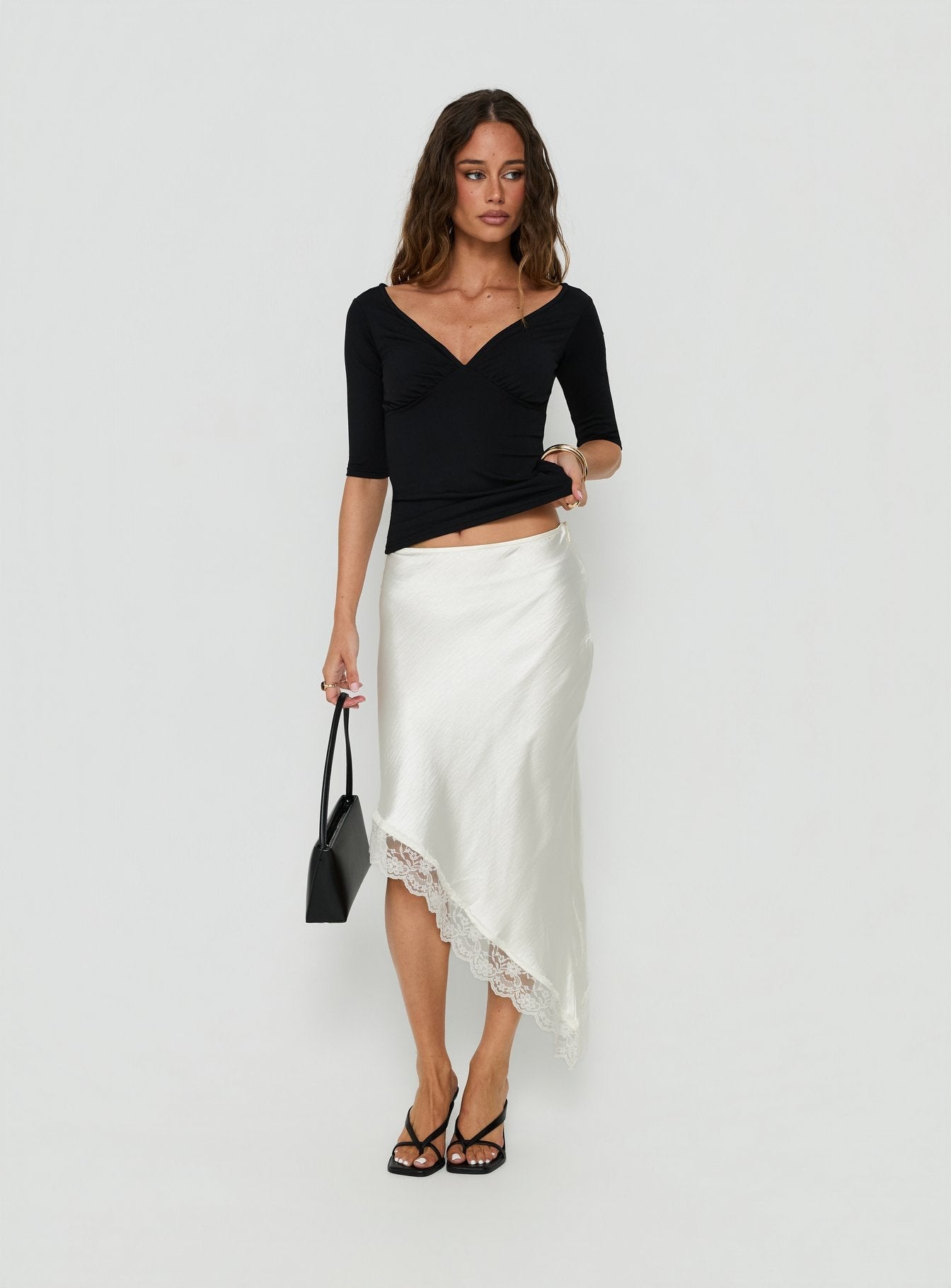 Featuring the Koletta Asymmetrical Lace Trim Satin Midi Skirt in Ivory with fitted silhouette front view of model wearing Princess Polly