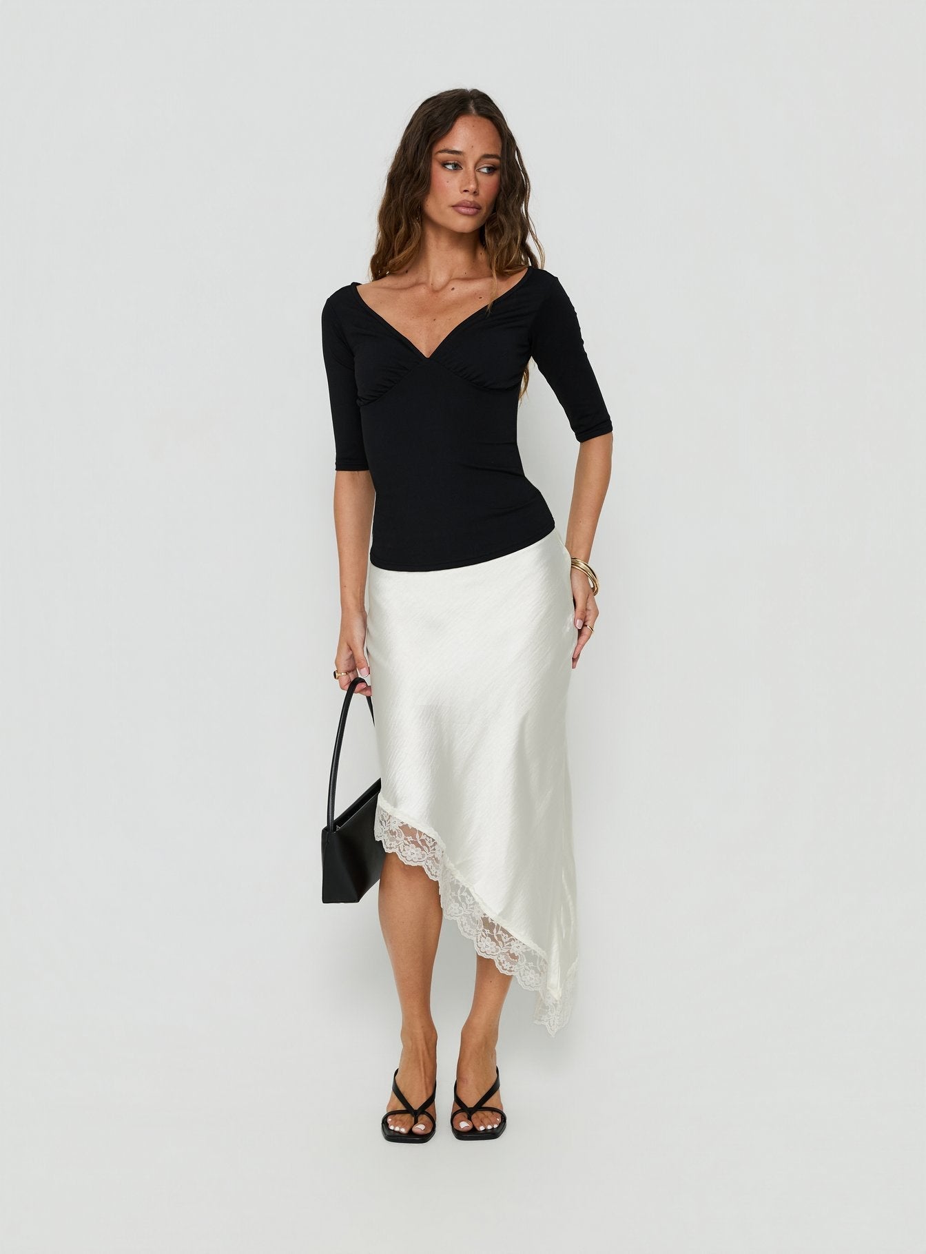 Featuring the Koletta Asymmetrical Lace Trim Satin Midi Skirt in Ivory with fitted silhouette front view of model wearing Princess Polly