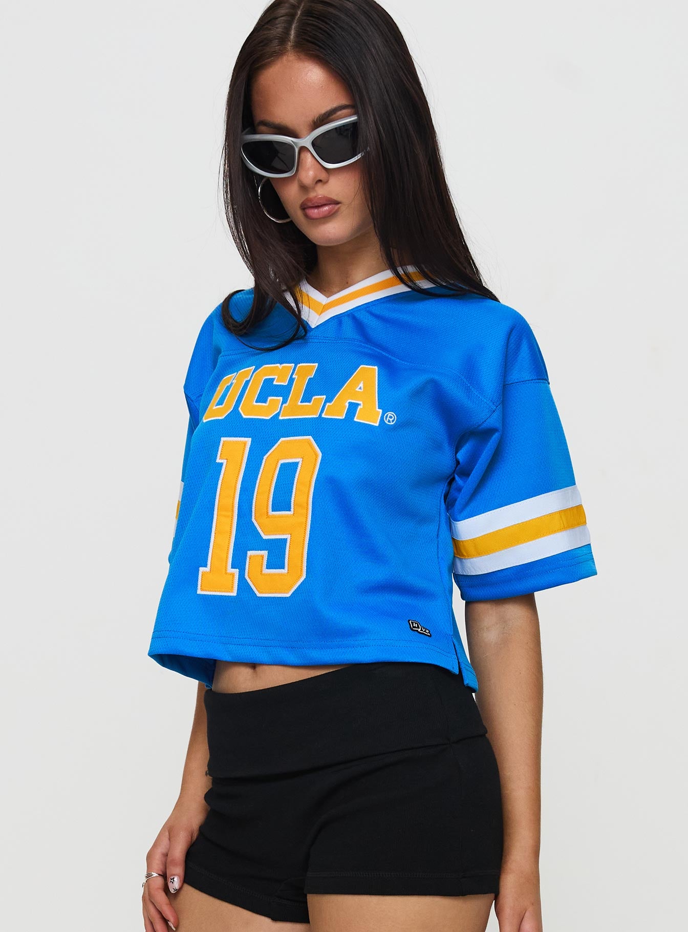 side view of model wearing Princess Polly UCLA Football Jersey Blue Half Sleeves V-Neck 