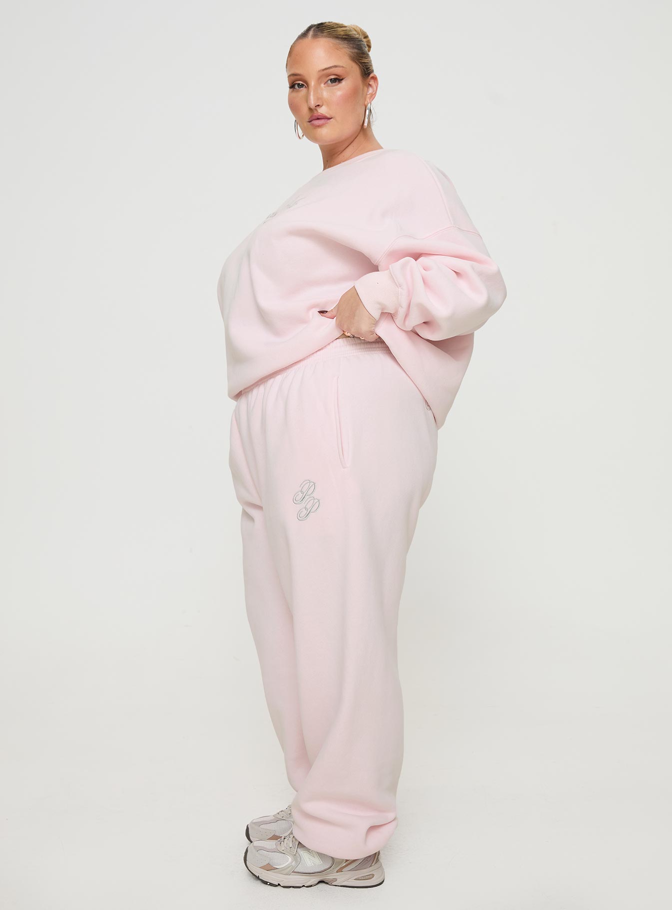 side view of model wearing Princess Polly Princess Polly Track Pants Script Baby Pink / Grey Curve 